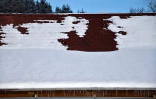 Roof with asphalt shingles covered with snow and icicles.